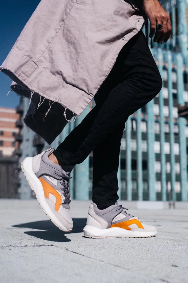 Detail of white and orange sneakers with black trousers.