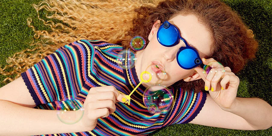 Reclining model wearing blue mirrored Spectacles and a striped shirt.
