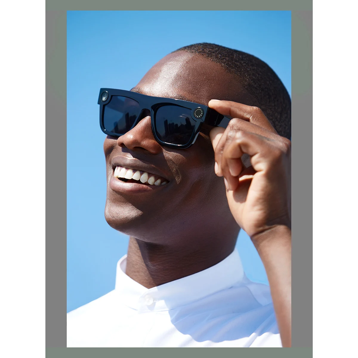 Smiling model adjusting Spectacles against a bright blue background.