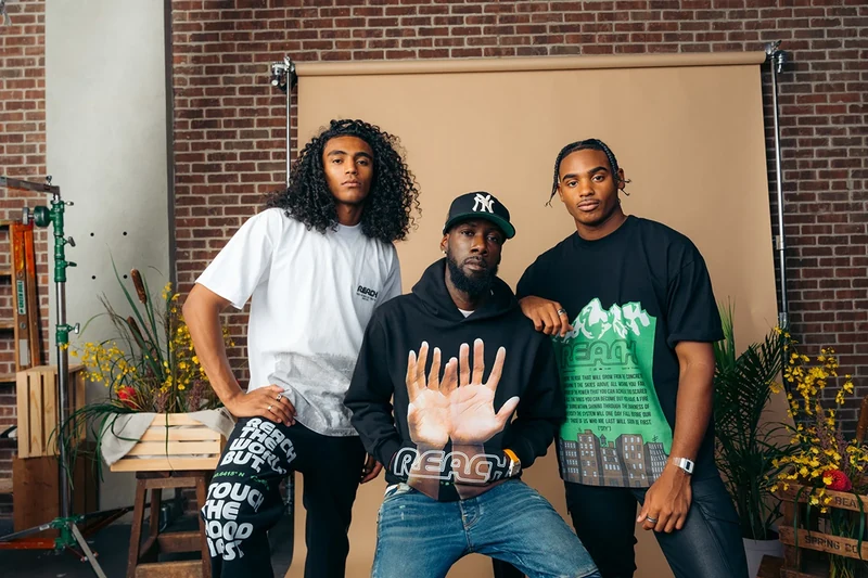Three models wearing printed tees and a black hoodie.