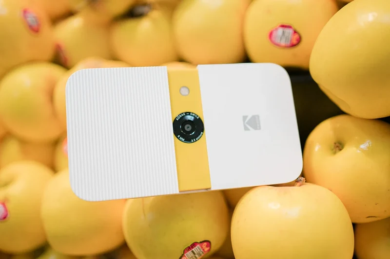 White and yellow Kodak camera among yellow apples.