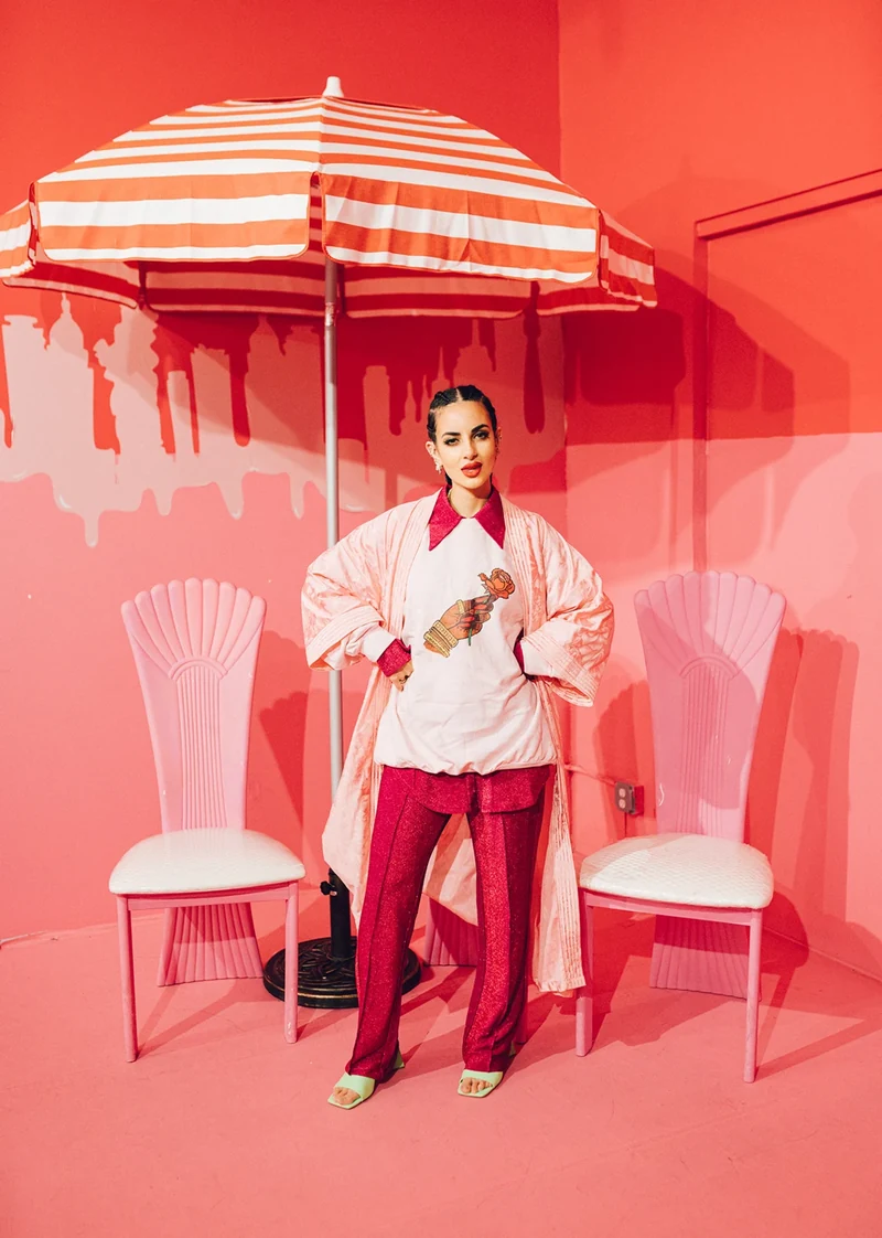 Pink tailoring and red trousers in a coral room with a striped parasol.
