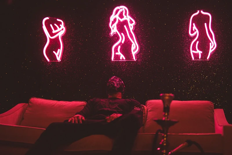 WRKINSILENCE reclining beneath pink neon figures.