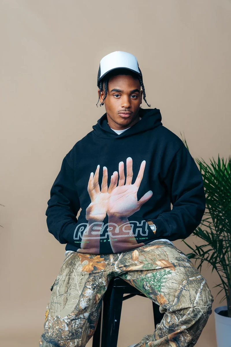 Model in a black hand-print hoodie and camouflage trousers.