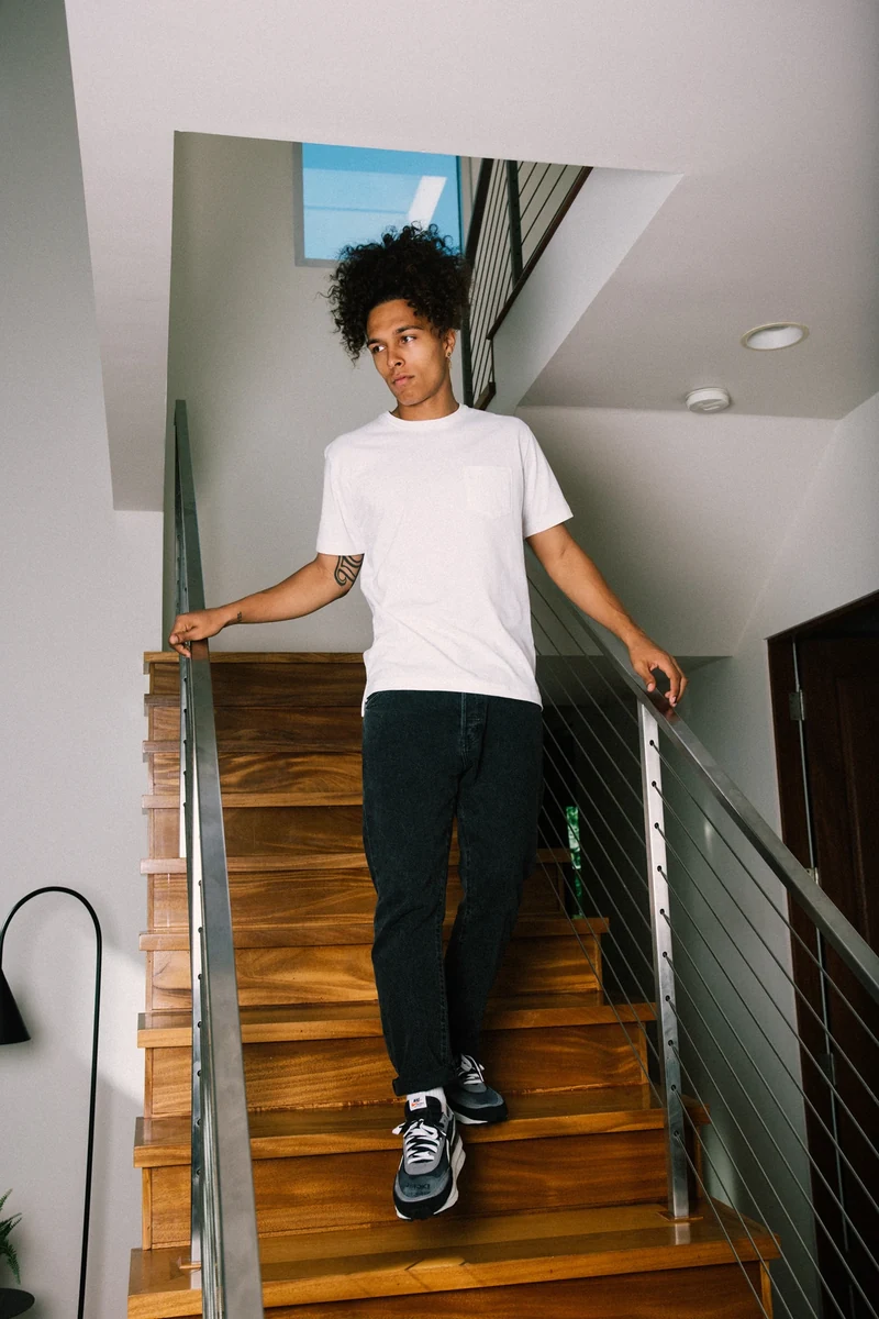 Model in a white tee standing on an indoor staircase.