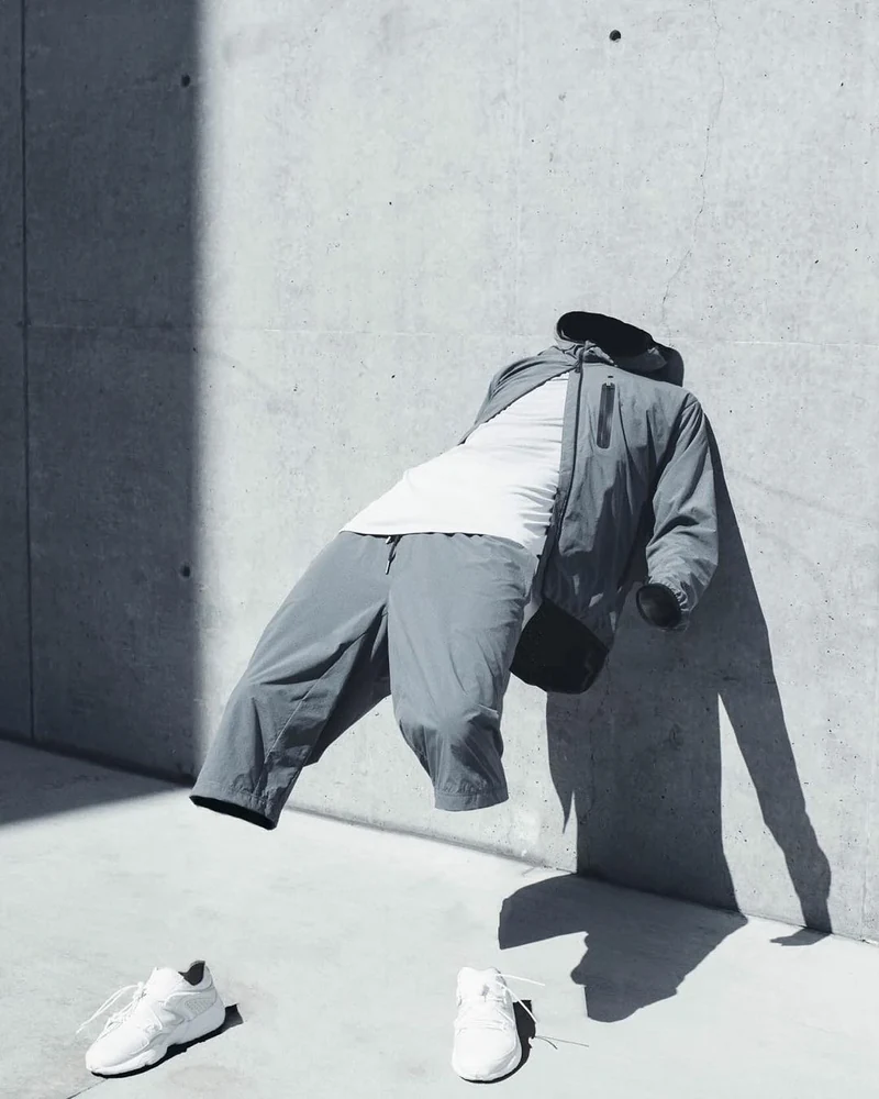 Model in a gray coat posed beside a concrete wall.