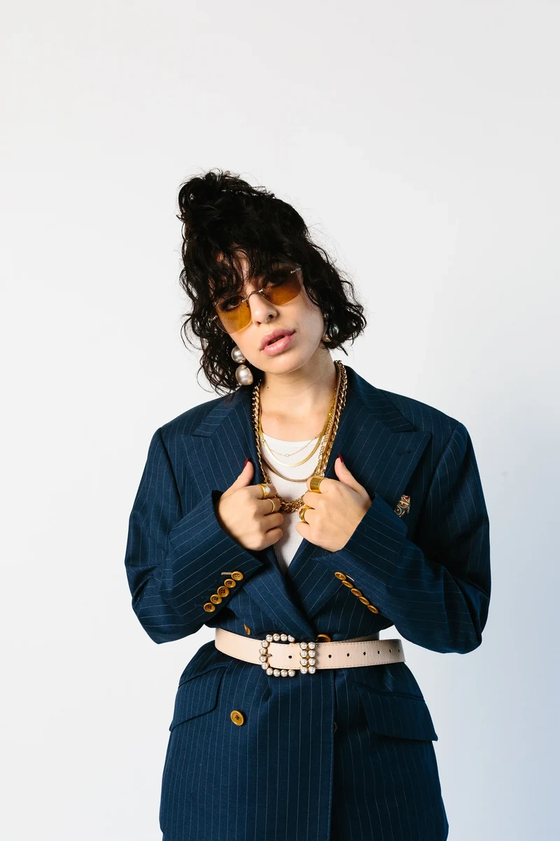 Close portrait of navy tailoring with a cinched waist and amber glasses.
