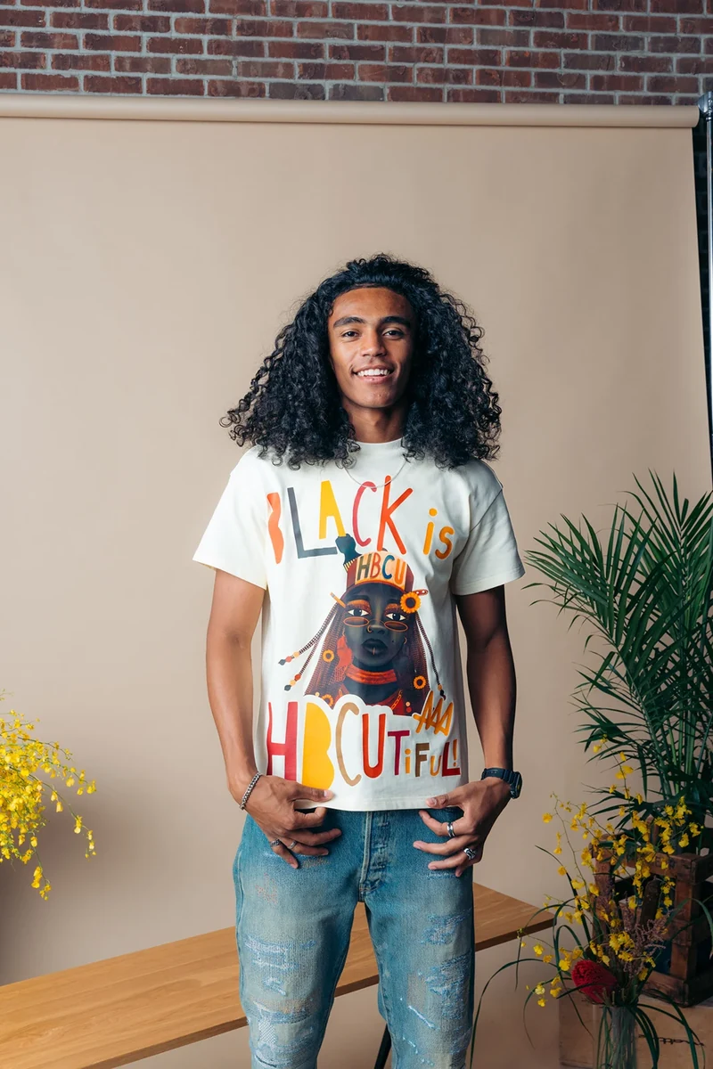 Model wearing a white graphic tee against a beige paper backdrop.