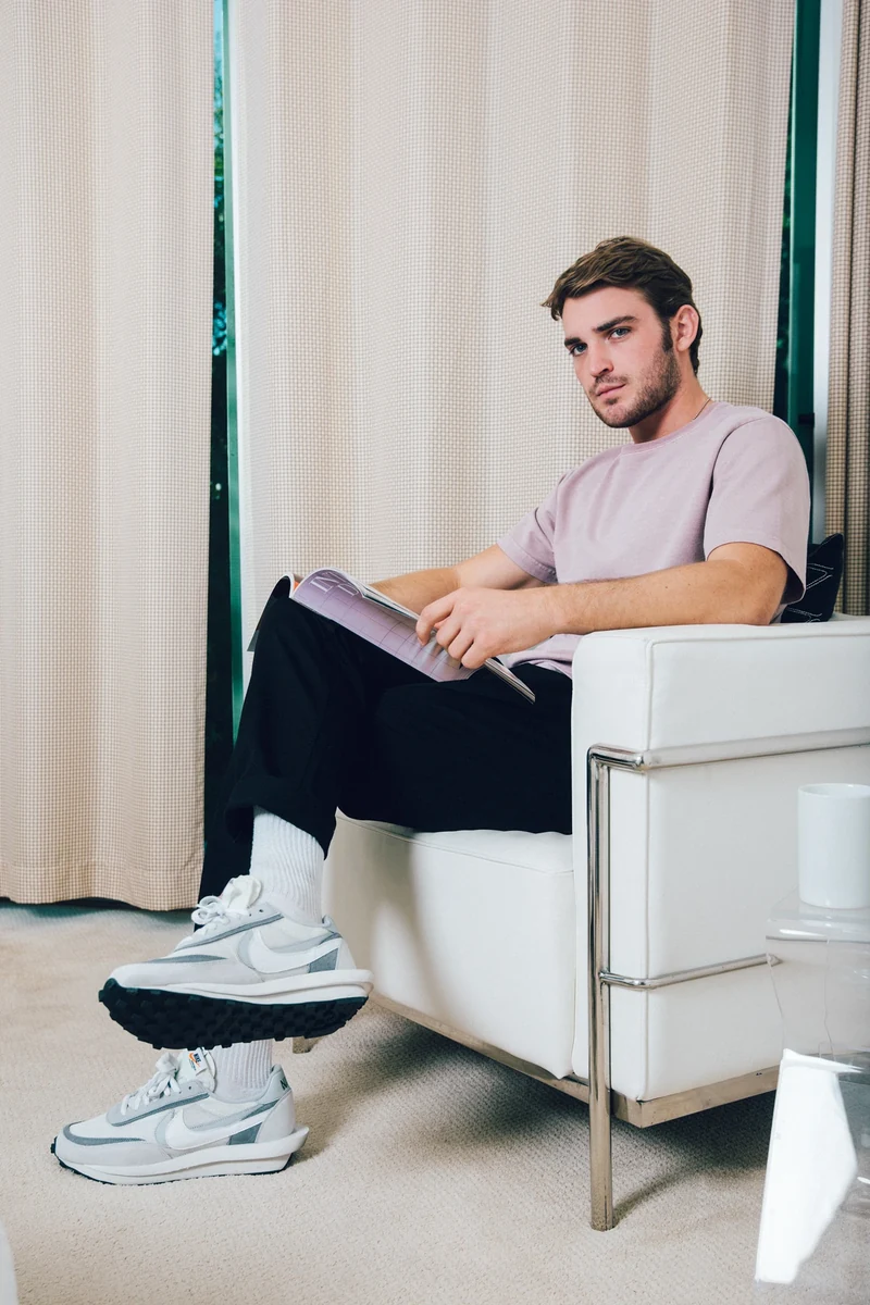 Model in a pale pink tee reading in an armchair.