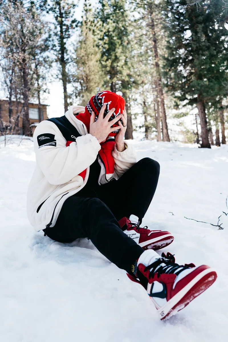 Seated model wearing the jacket with red sneakers in the snow.