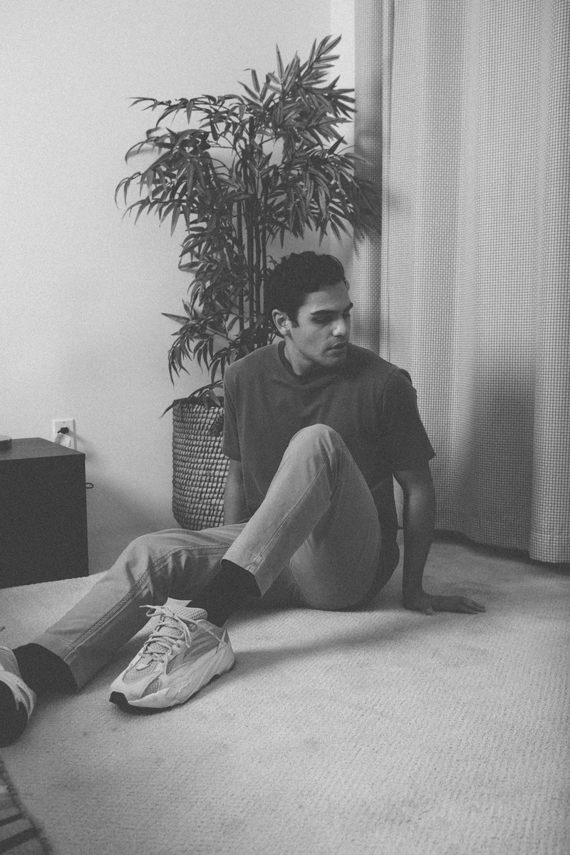 Monochrome seated portrait in a blue tee beside a plant.