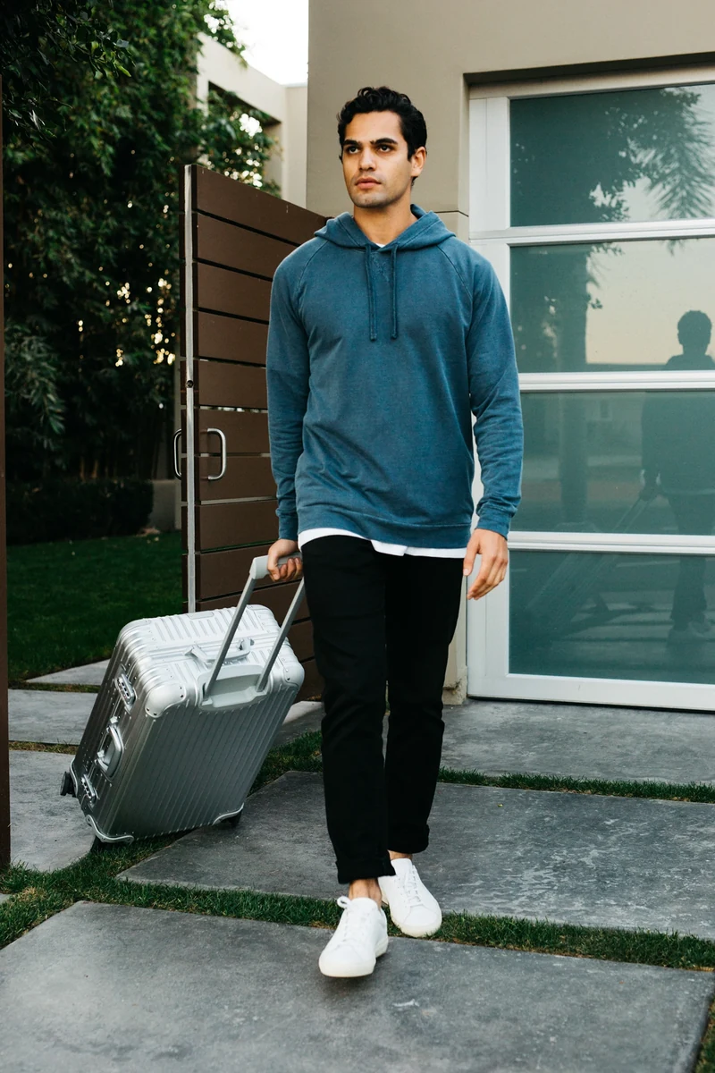 Model in a blue hoodie walking with a suitcase.