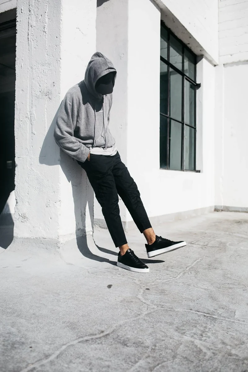 Model in a gray hoodie leaning against a white rooftop wall.