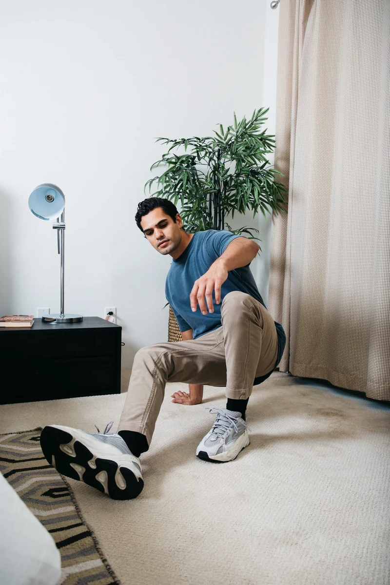 Model in a blue tee seated beside a potted plant.