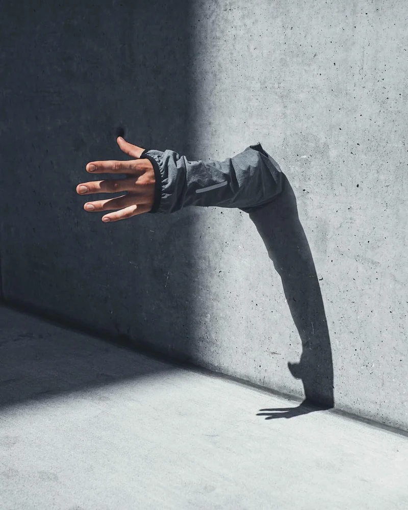 An outstretched arm emerging from behind a concrete column.