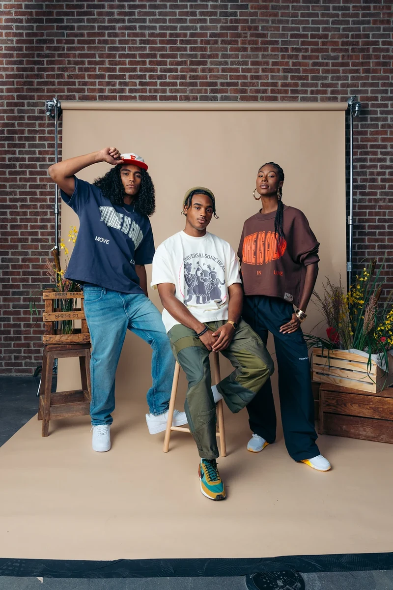 Three models in coordinated graphic tees on a beige studio set.
