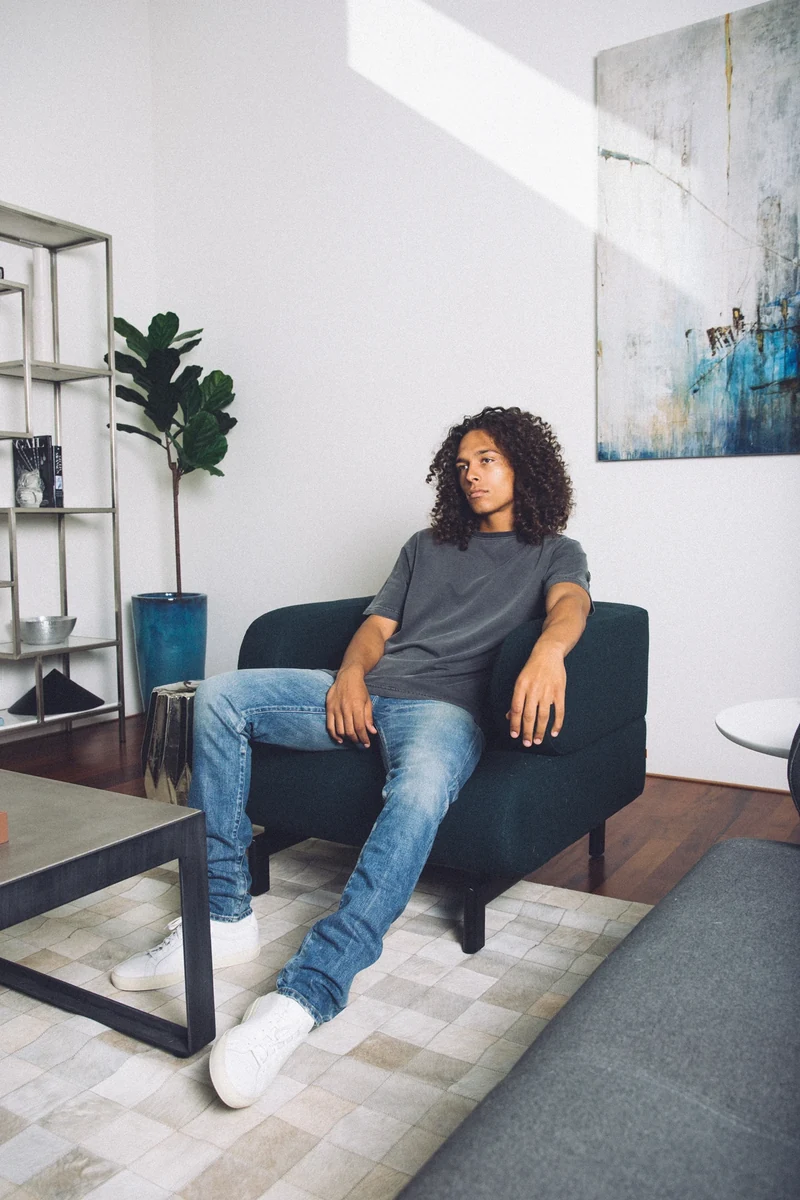 Model in a gray tee seated in a navy armchair.