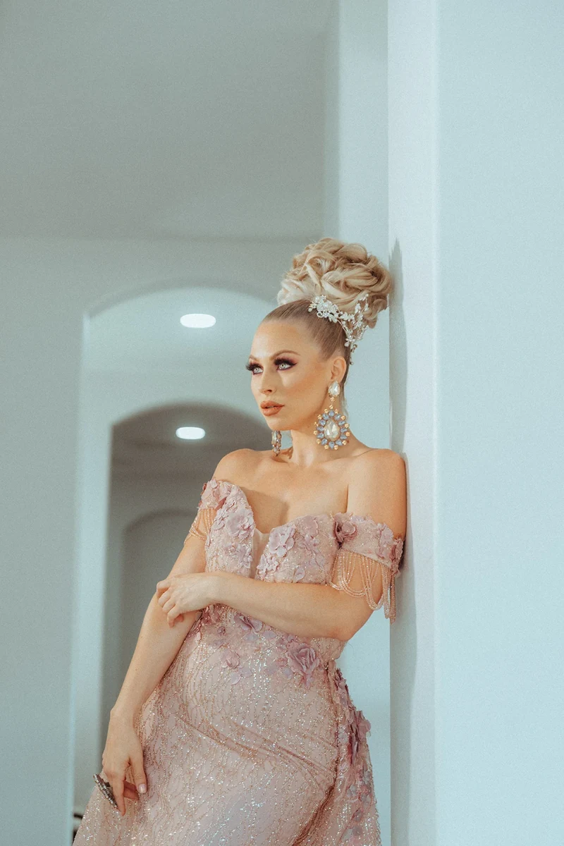Pastel beauty portrait in a pink dress against a pale blue doorway.