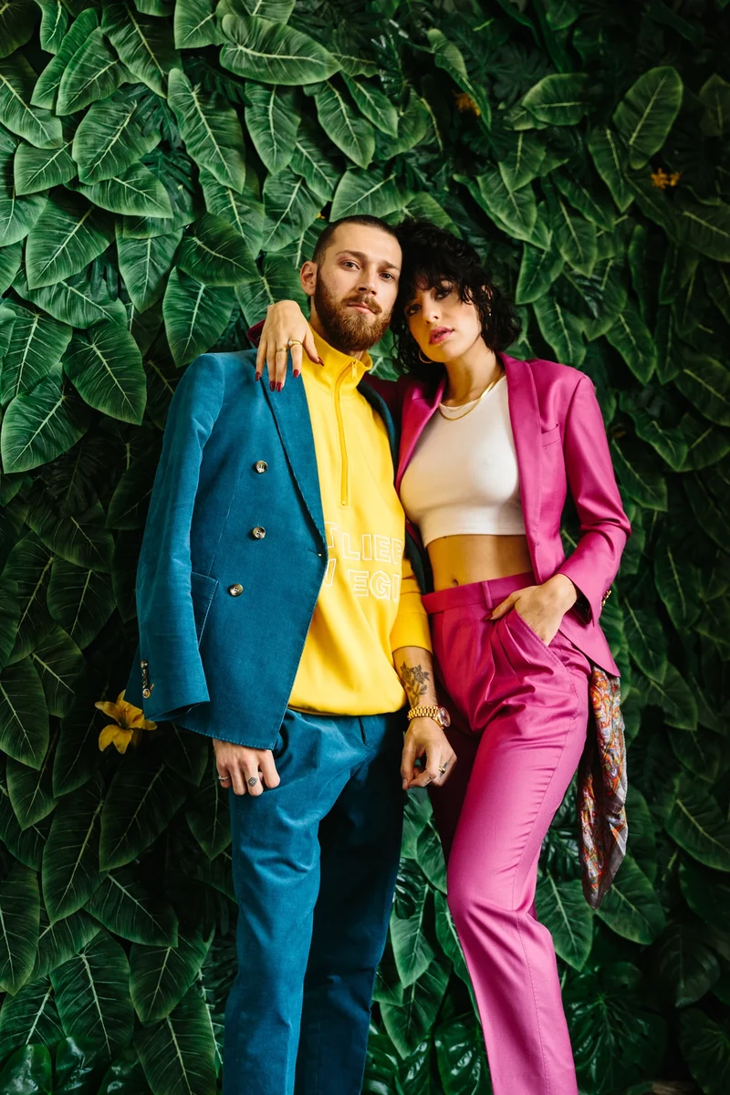Two models in teal and magenta tailoring against foliage.