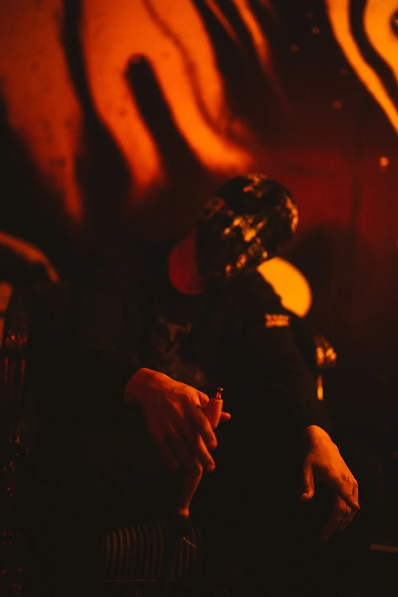 Close portrait of masked WRKINSILENCE in orange light.