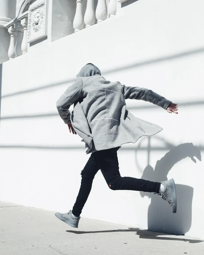 Model in a gray coat moving beside a white architectural wall.