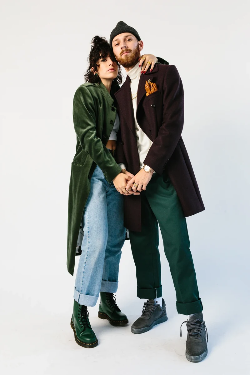 Two models together in green and dark tailoring against a white backdrop.