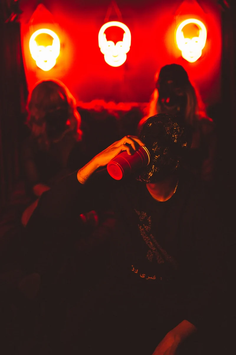 Masked WRKINSILENCE portrait under red and yellow neon.