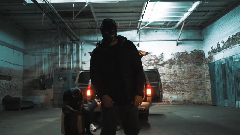 WRKINSILENCE in a cool-lit warehouse, with a vehicle behind him.