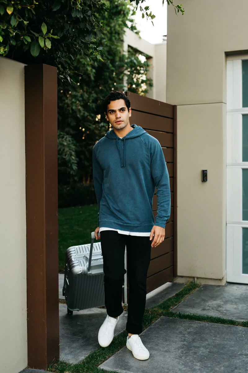 Model in a blue hoodie outside a house.