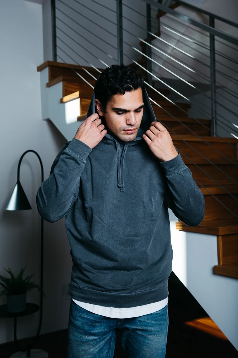 Model adjusting the hood of a dark sweatshirt beside a staircase.