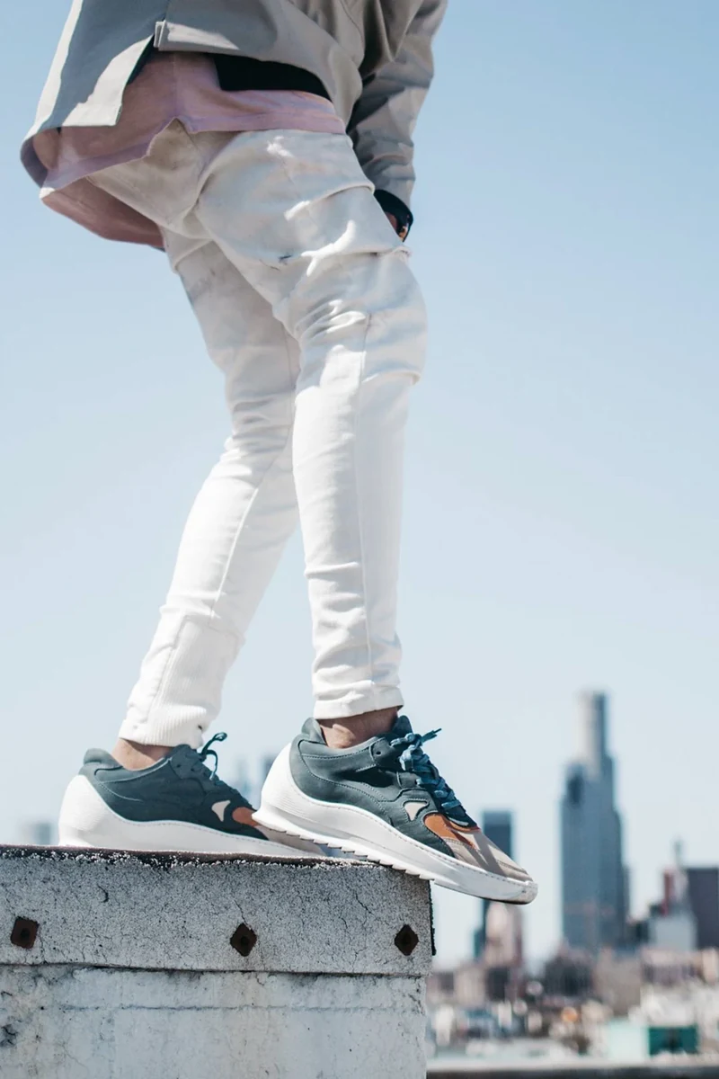 Close view of sneakers and pale trousers on a rooftop ledge.