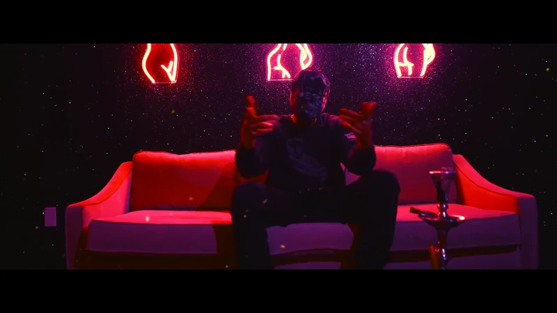 WRKINSILENCE seated on a red couch beneath purple and red neon lights.