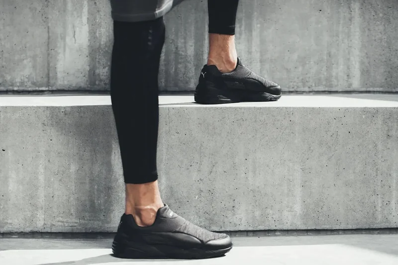 Black sneakers and cropped trousers on concrete steps.