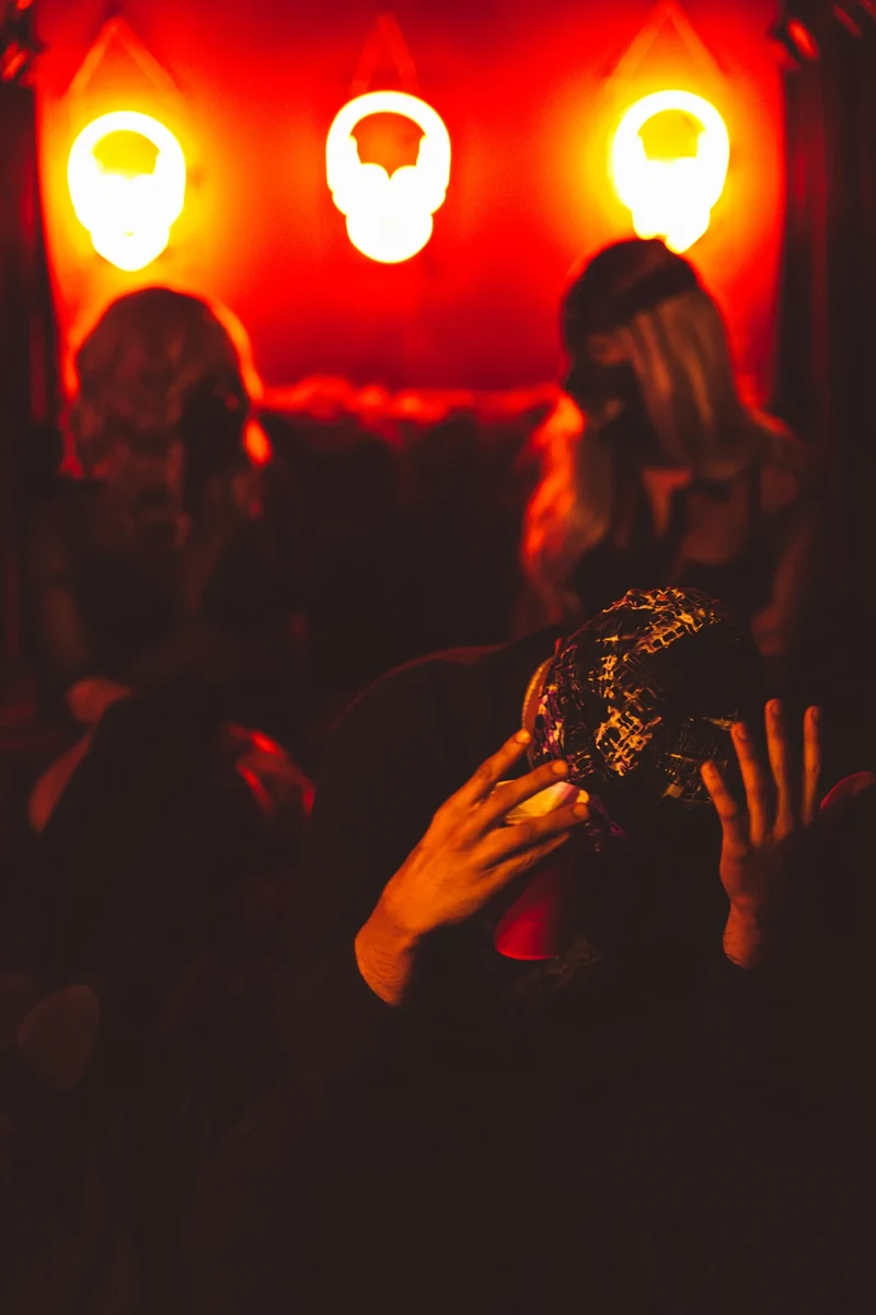 WRKINSILENCE with hands raised beneath neon skull lights.