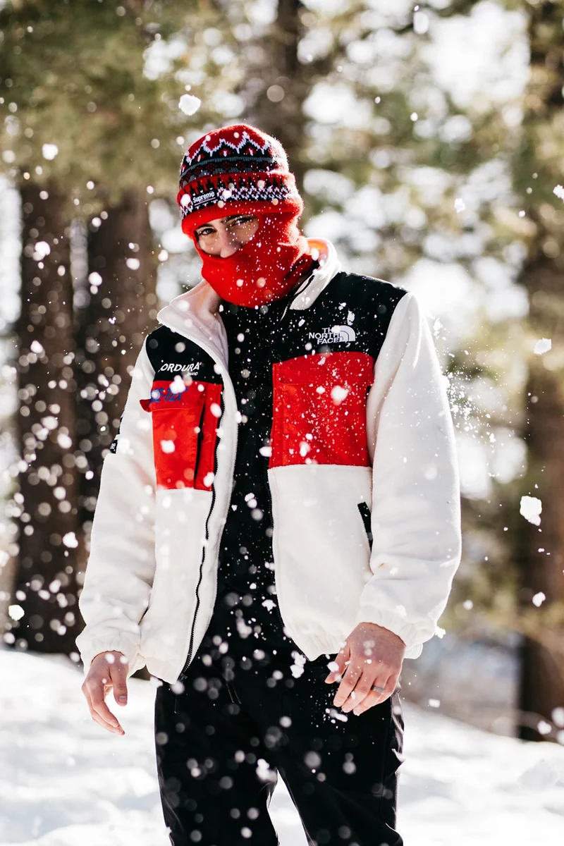 Model wearing a white, red, and black North Face jacket in falling snow.